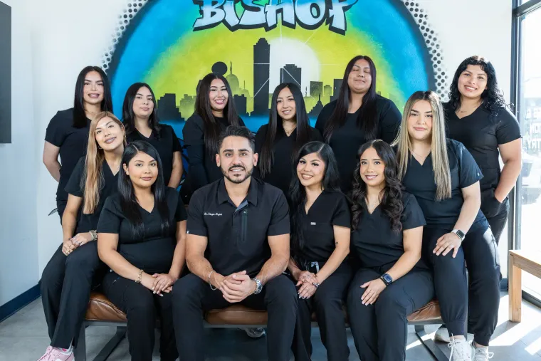 The Arts Family Dentistry team in black scrubs in front of the hand-painted Bishop Arts Dallas skyline mural