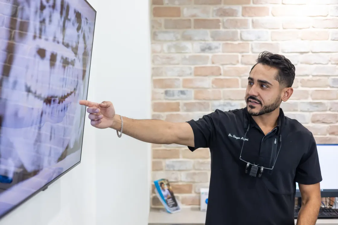Dr. Shayan Azimi pointing to a patient's full-mouth x-ray on a wall-mounted screen in a treatment room
