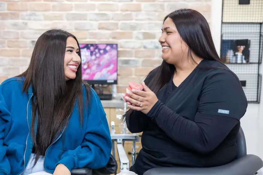 A team member showing a patient a dental model in a treatment room with exposed brick walls