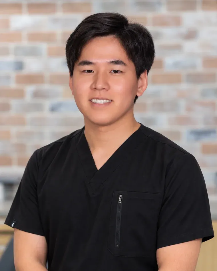 Dr. Brian Hwangpo, pediatric dentist at Arts Family Dentistry, in black scrubs against the practice's brick wall