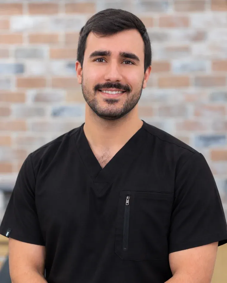 Dr. Farbode Karimi, general dentist at Arts Family Dentistry, in black scrubs against the practice's brick wall