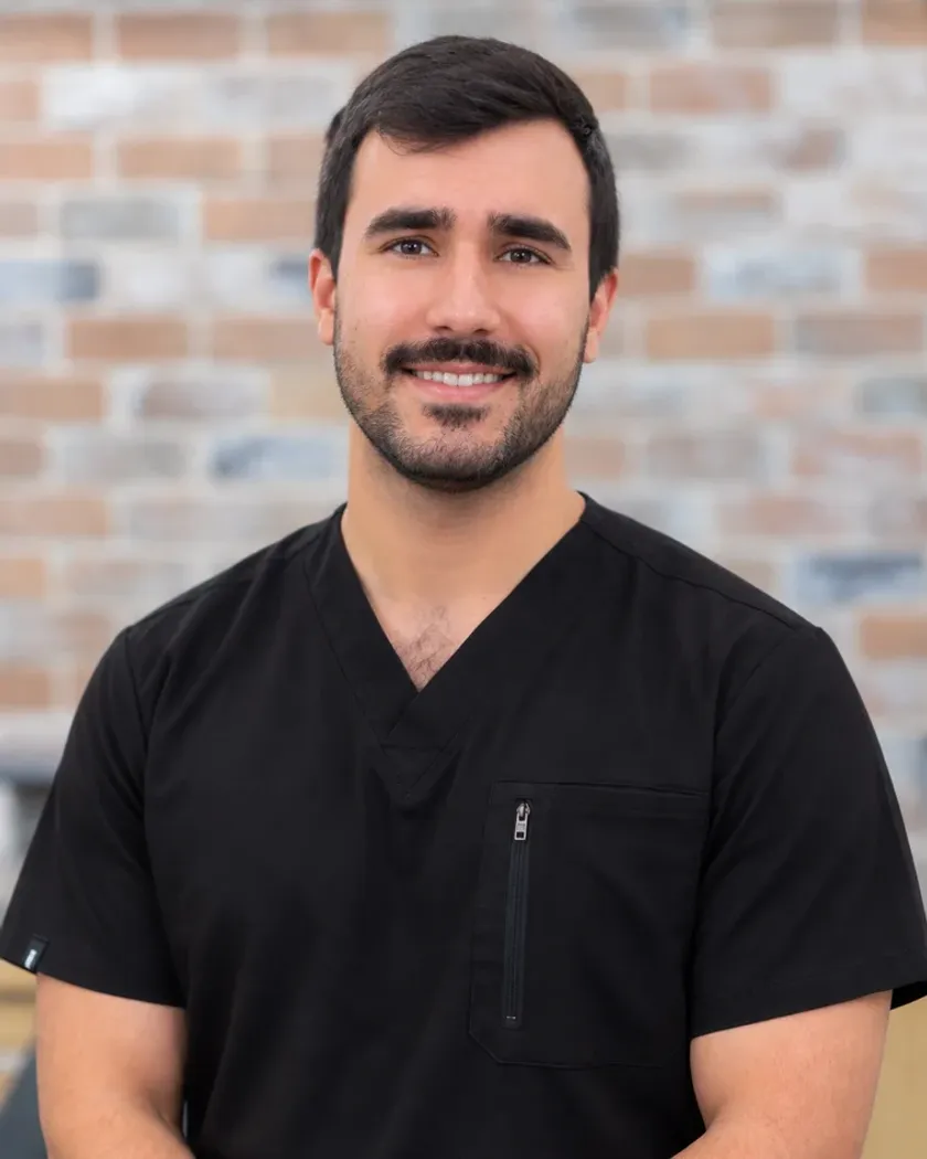 Dr. Farbode Karimi, general dentist at Arts Family Dentistry, in black scrubs against the practice's brick wall