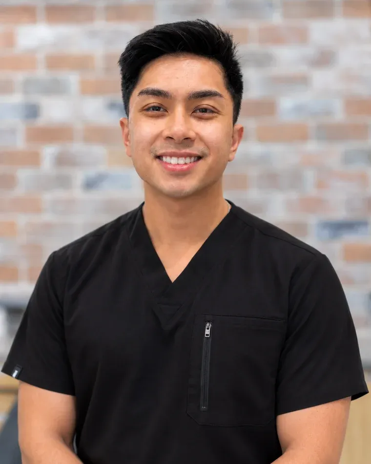 Dr. Jason Nguyen, orthodontist at Arts Family Dentistry, in black scrubs against the practice's brick wall