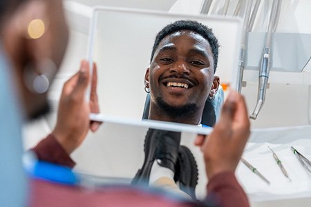 Man smiling at reflection in handheld mirror