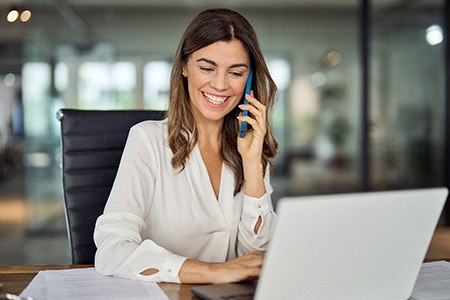 Smiling woman talking on phone and working on laptop