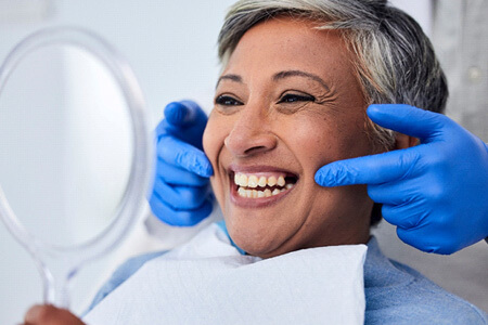 woman smiling at reflection in handheld mirror