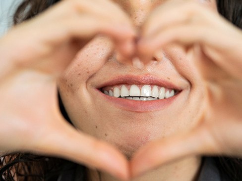 Woman using her hands to make a heart shape around her smile