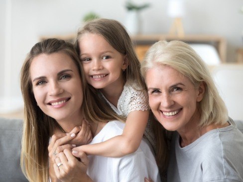 Three generations of women smiling after dental implant tooth replacement