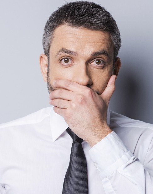 Man in need of replacement for missing teeth covering mouth