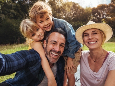 Smiling family of four outdoors after screening for traditional orthodontics