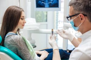 Dentist holding up a dental implant to a patient.