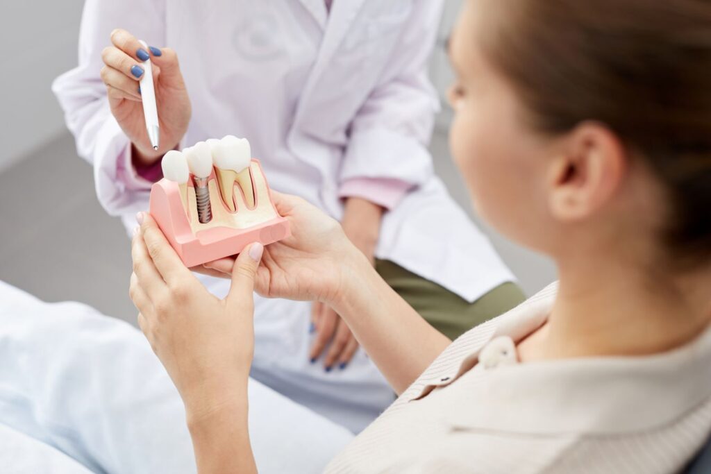 A dentist showing a woman a model of a dental implant in the jaw