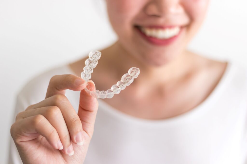 Chin-to-chest view of woman in white shirt holding Invisalign