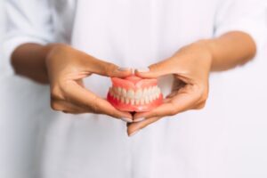 Person in white jacket holding set of dentures.