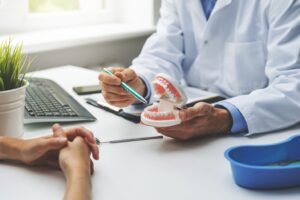 Dentist pointing to model of mouth on his desk during consultation.